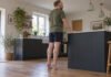Tendinopathie d’Achille : pourquoi le massage seul ne suffit pas Homme effectuant une élévation des talons sur sol plat avec appui léger sur un comptoir.