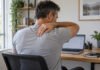 Douleur entre les omoplates : cou, thorax, épaule ou simple fatigue musculaire ? Homme faisant une pause au bureau, une main sur le haut du dos.