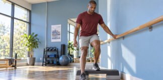 Homme effectuant un exercice contrôlé sur une marche basse avec appui sur une barre.