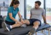 Traitement manuel avant une compétition : peut-il réellement améliorer la performance ? Traitement manuel doux de la jambe d’un sportif dans une salle de préparation près d’une piste d’athlétisme.